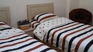 Een hotelkamer met twee bedden, elk voorzien van gestreepte lakens, een klein bijzettafeltje met een plantje en een stoel.