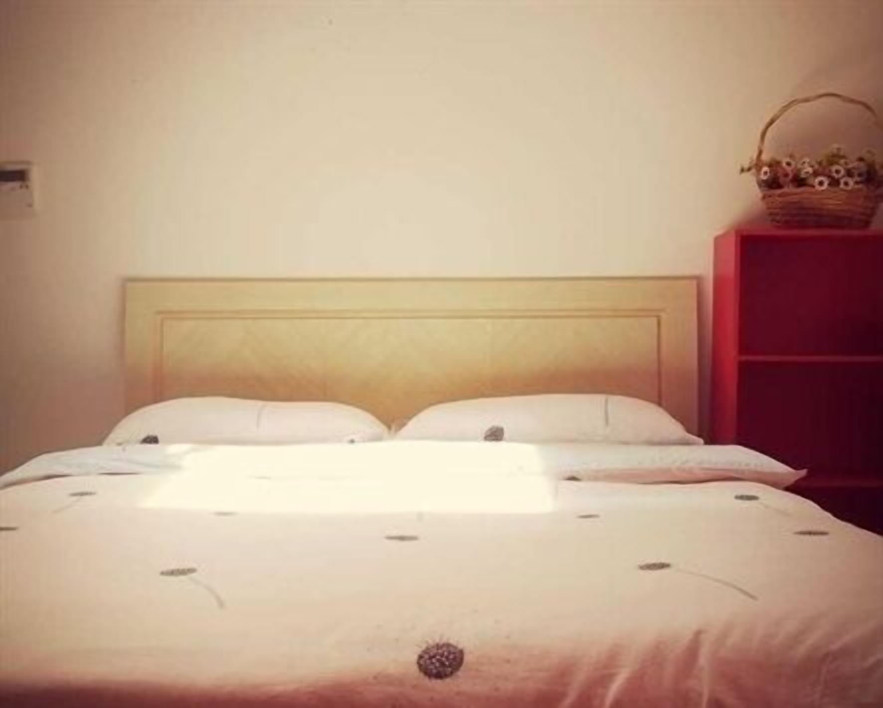 A bed with a wooden headboard, white bedding, and a basket on a red shelf beside it.
