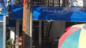 Un callejón estrecho con un toldo azul que dice “Amber” y un paraguas de playa colorido.