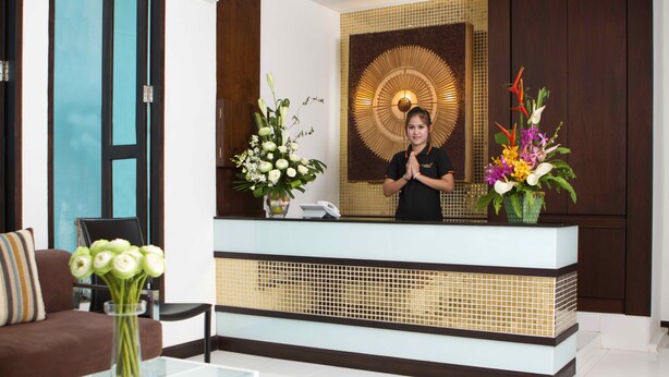 Zona de recepción con diseño moderno, que incluye un mostrador de recepción, un sofá y una mesa de centro con un jarrón de flores.