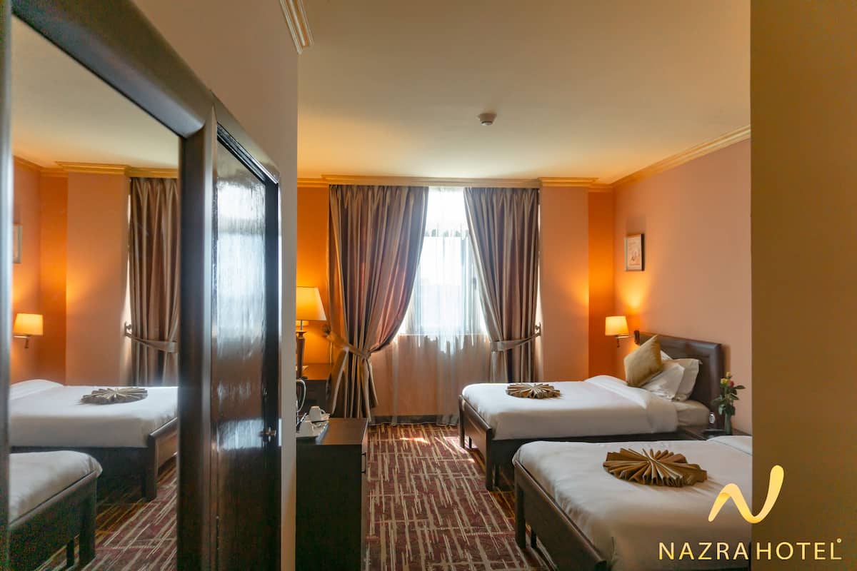 A hotel room with two beds, a large mirror, a desk, and a window with curtains.