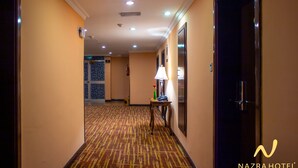 A hotel corridor with patterned carpet, a table with a lamp, and an exit sign. - Nazra Hotel (Addis Ababa)