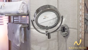 A bathroom with a towel rack holding a folded towel, a wall-mounted toilet with a transparent lid, and a decorative tile border. - Nazra Hotel (Addis Ababa)