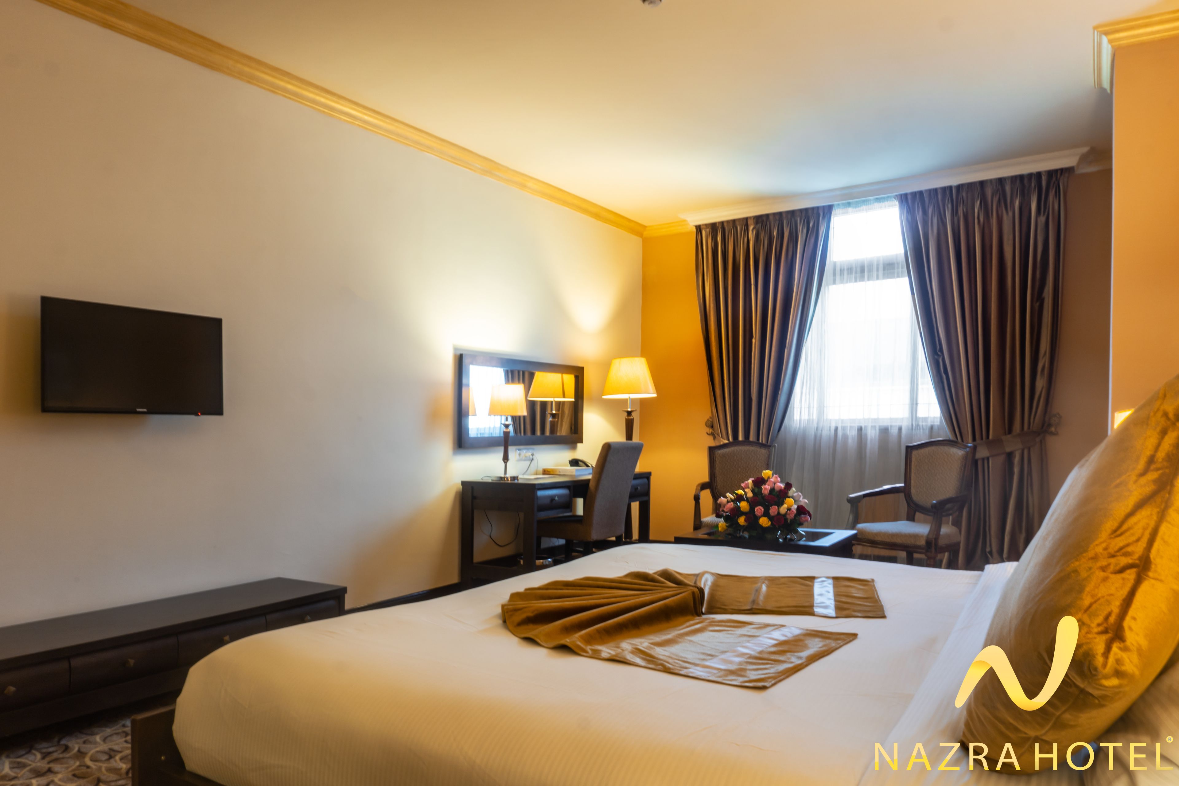 A hotel room with a bed, a desk, a chair, a television, and a window with curtains.