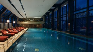 A modern indoor swimming pool with sun loungers and large windows offering city views. - IFC Residence (Shanghai)