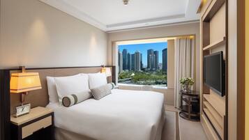 Habitación de hotel con una cama grande, televisión, mesita de noche con lámpara y vistas a la ciudad.