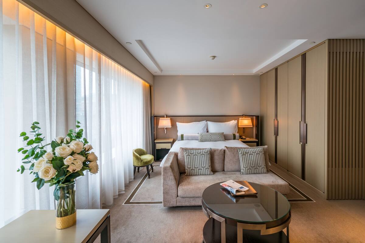 Una habitación de hotel moderna con cama, lámparas de noche, un sofá, una mesa de centro de cristal y un jarrón de flores.