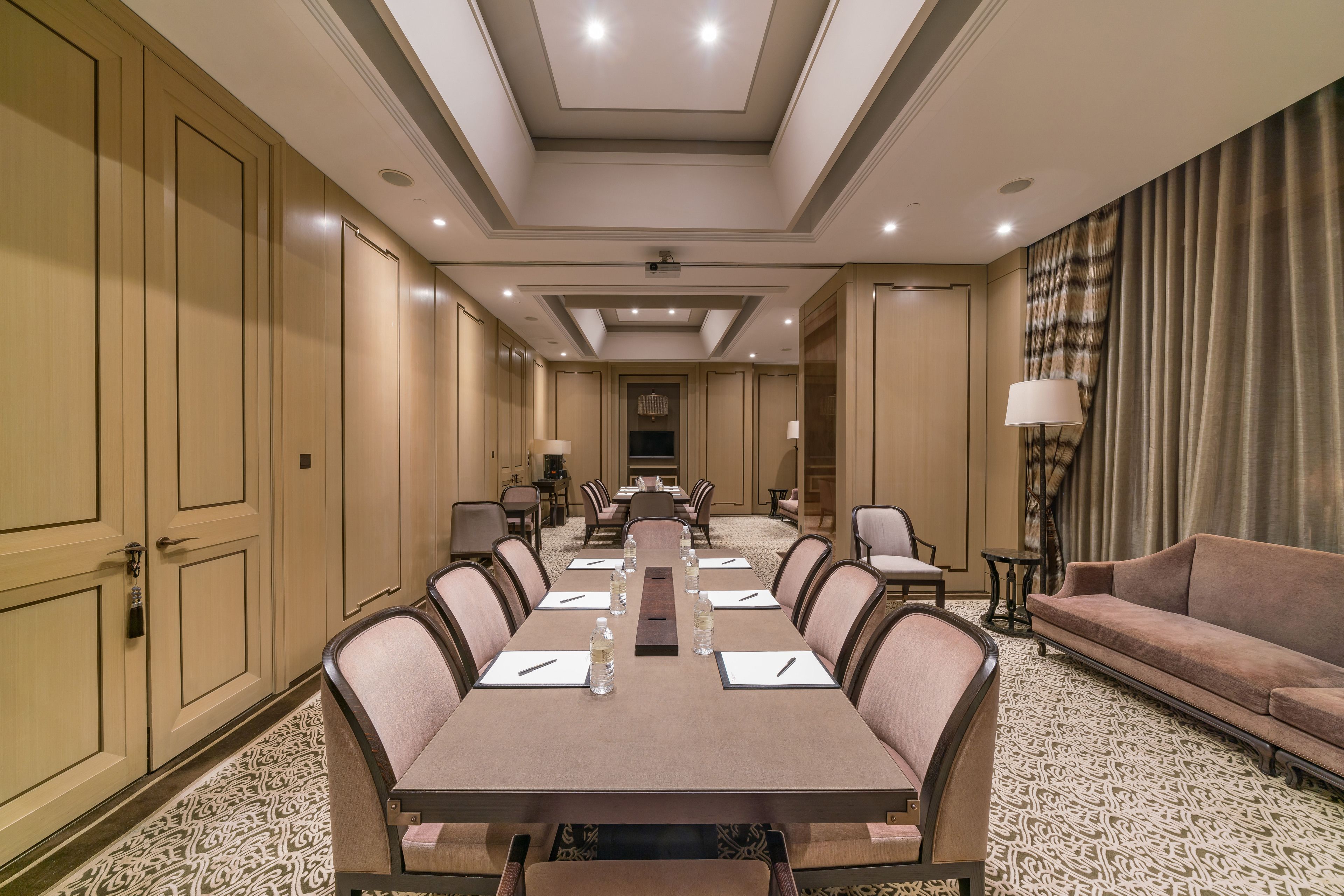 A conference room with a long table, chairs, a sofa, and a lamp.