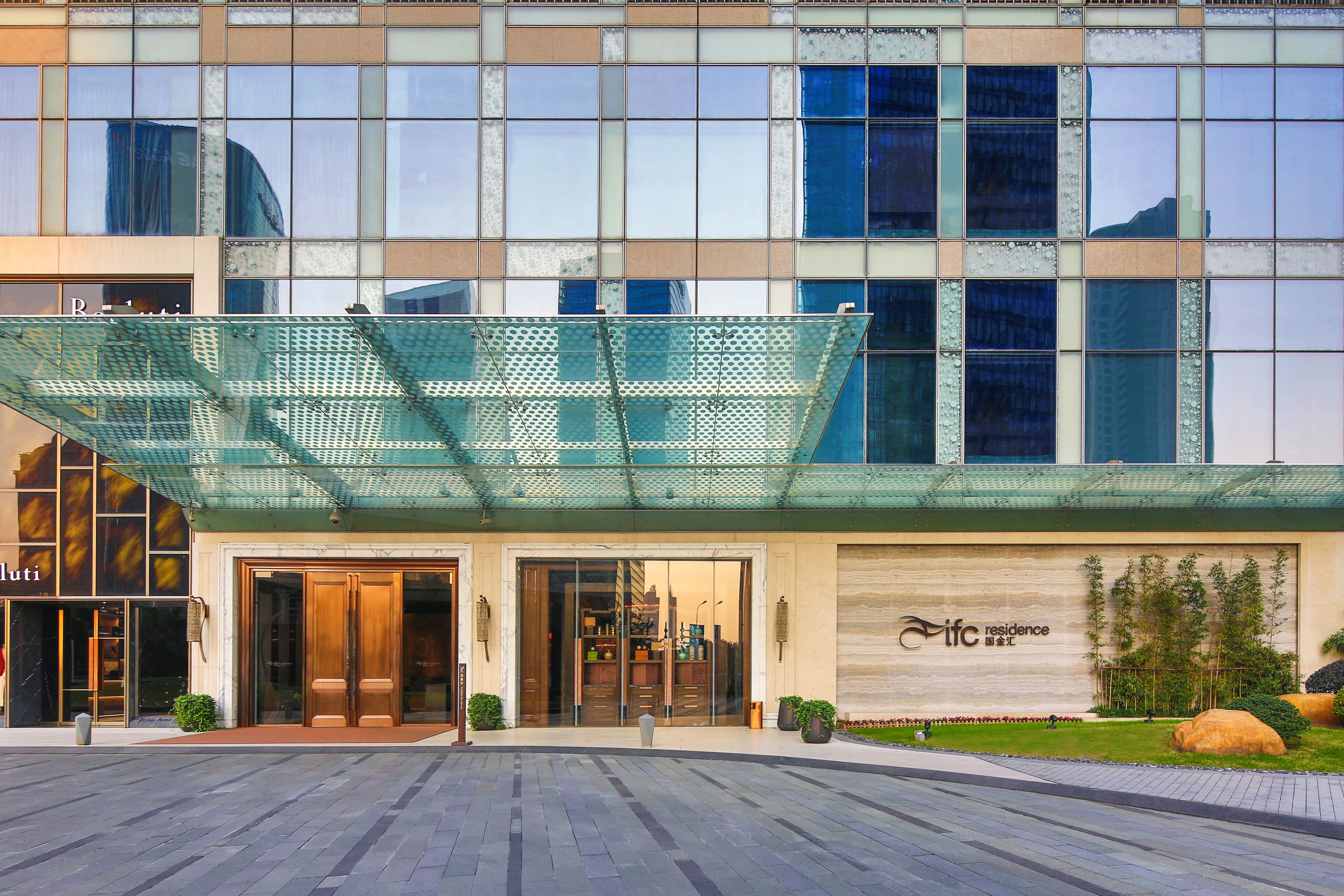 Una entrada de hotel moderna con fachada de vidrio, un área de acceso cubierta y un letrero que dice "ITFC Residence".