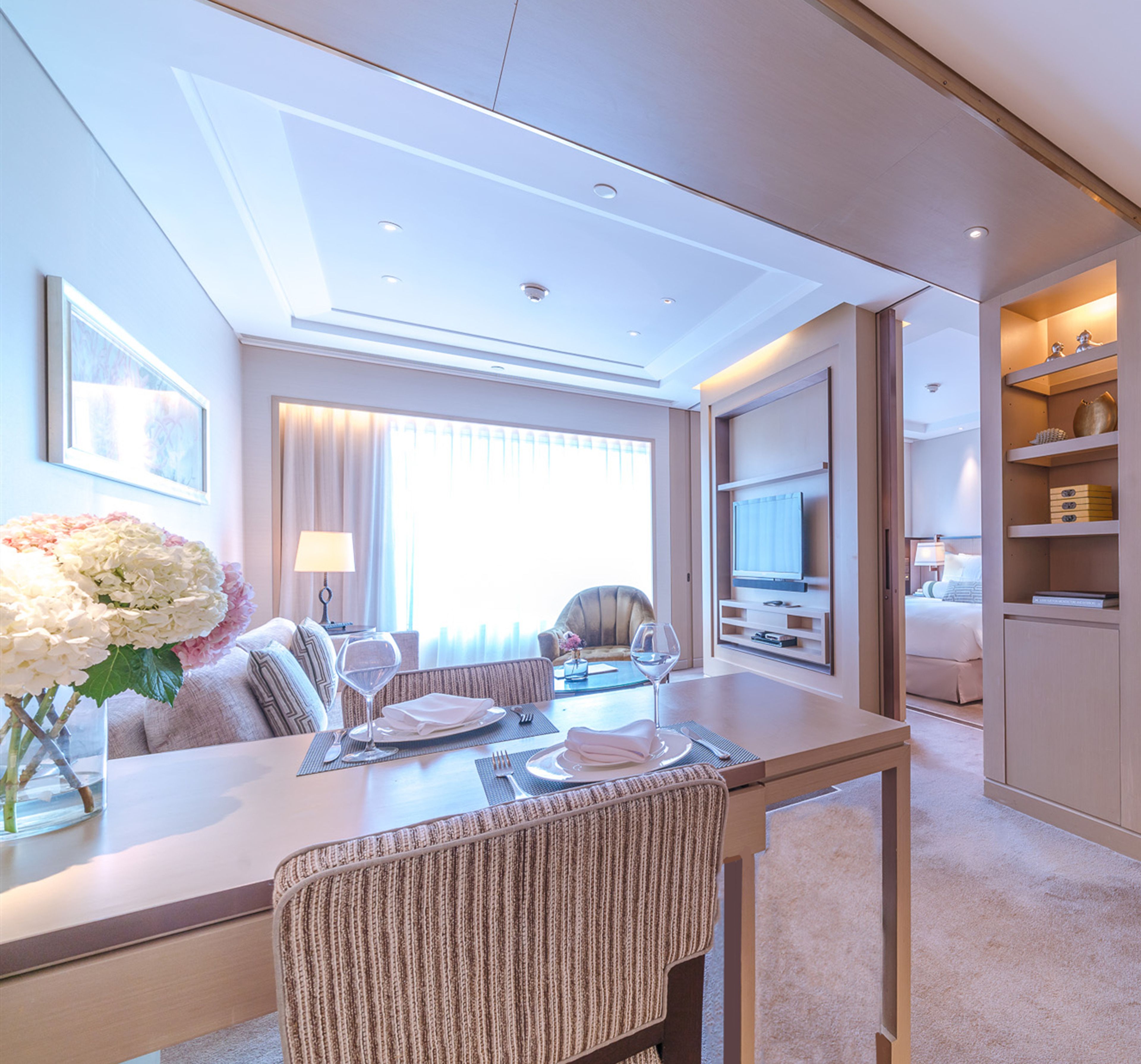A modern hotel room with a dining area, a TV, and a minibar.
