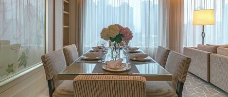 A hotel dining room with a glass table, six chairs, a vase of flowers, and a sofa in the background.