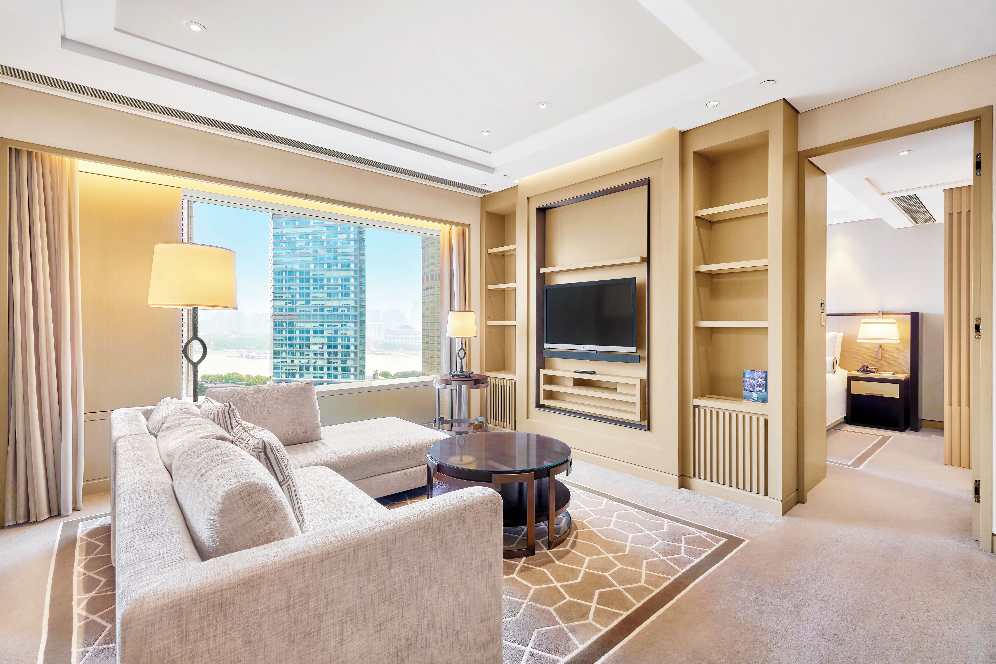 A modern hotel room with a sofa, two lamps, a TV, and a view of a cityscape.