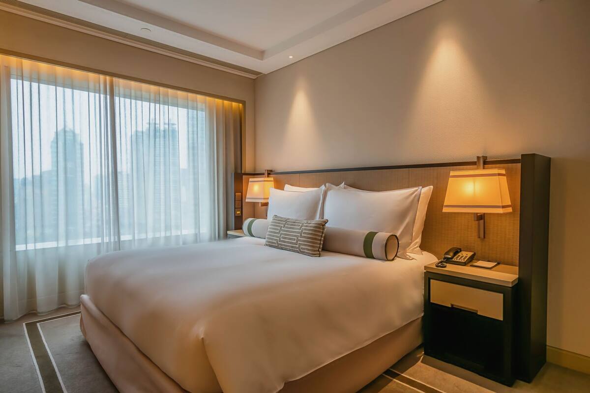Habitación de hotel con una cama grande, dos lámparas de noche, un teléfono y una ventana con cortinas.