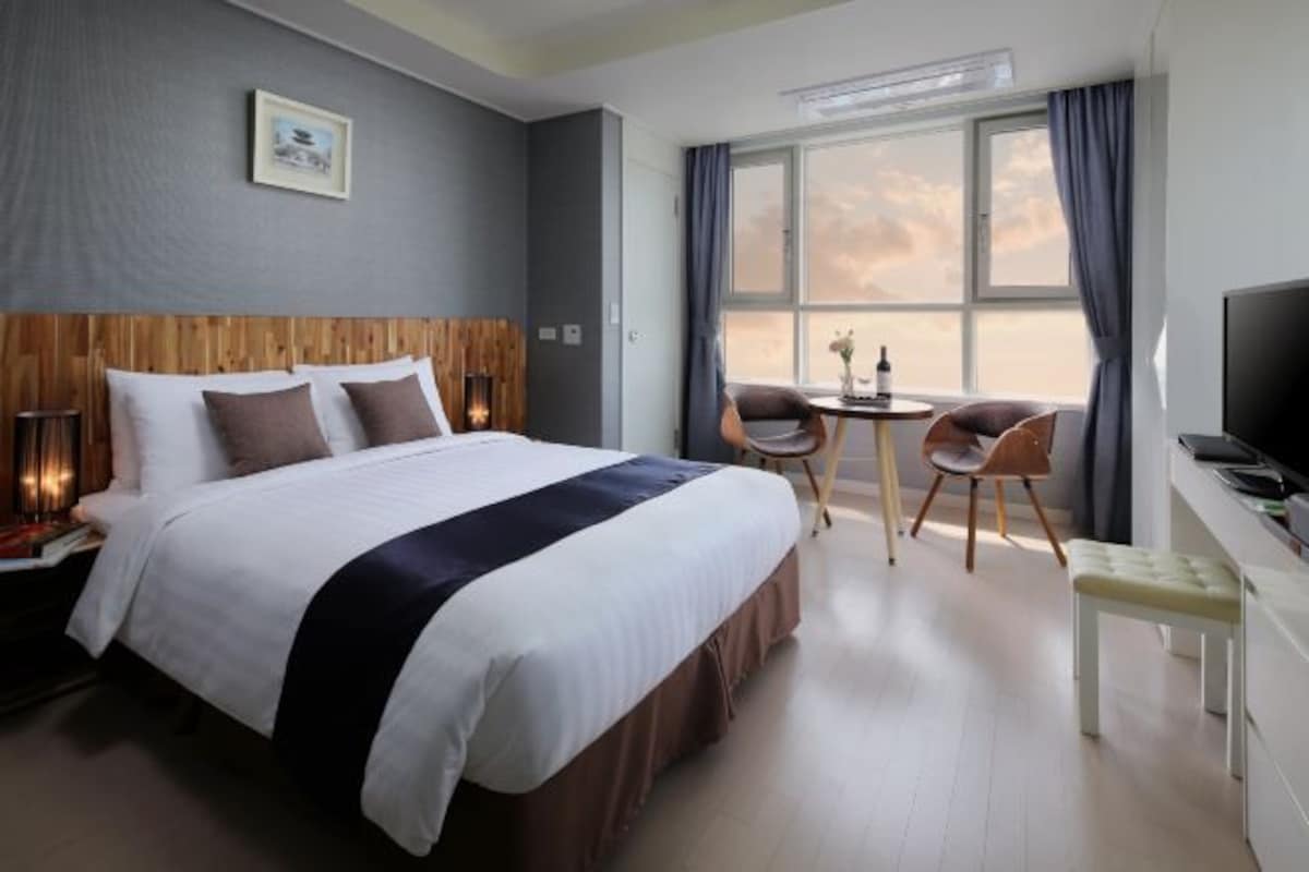 A hotel room with a large bed, a desk with a chair, a television, and a window with curtains.