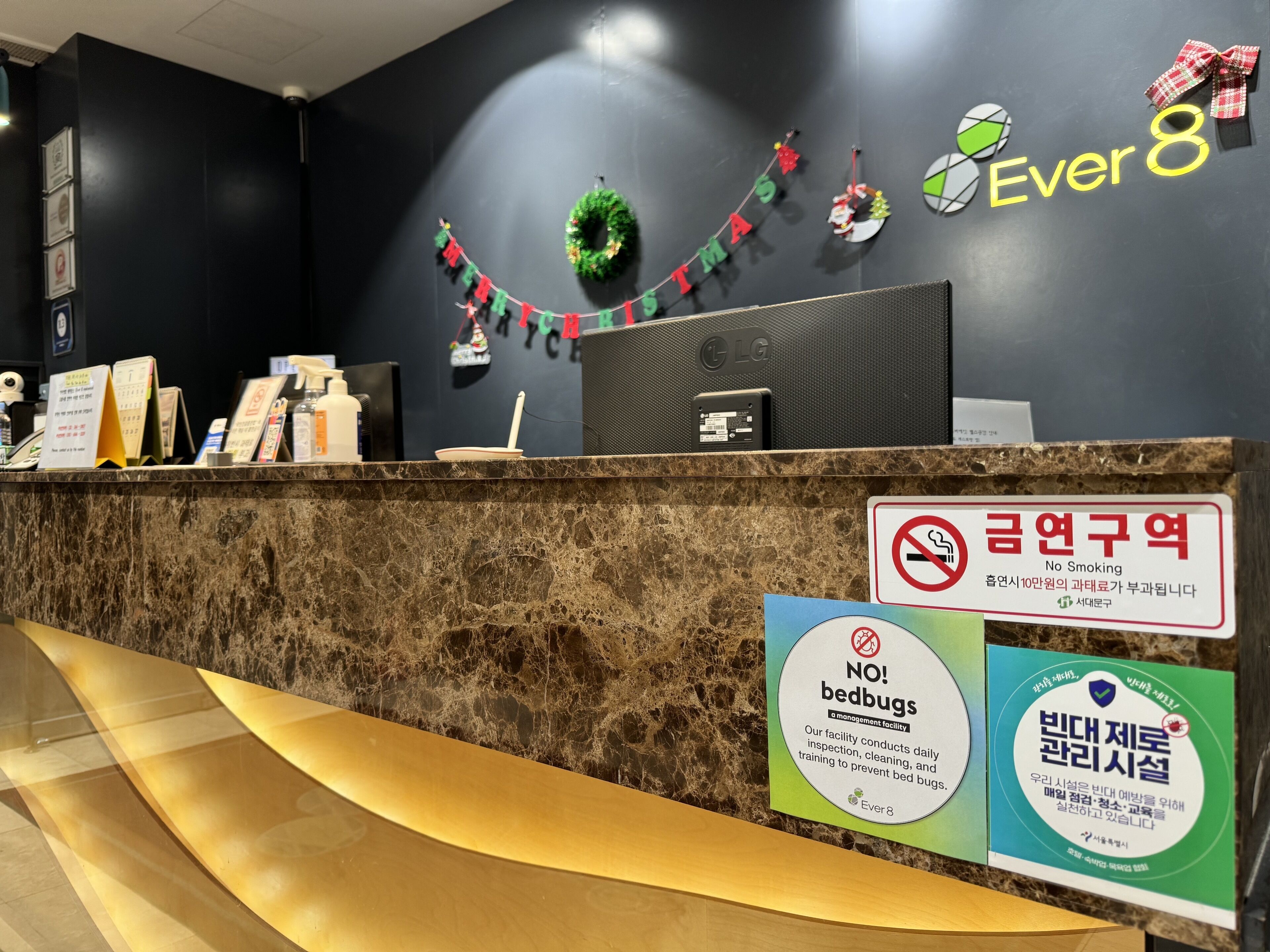 A hotel reception desk with a marble counter, a 'No Smoking' sign, and 'No Bedbugs' and 'Bedbug Inspection' signs.