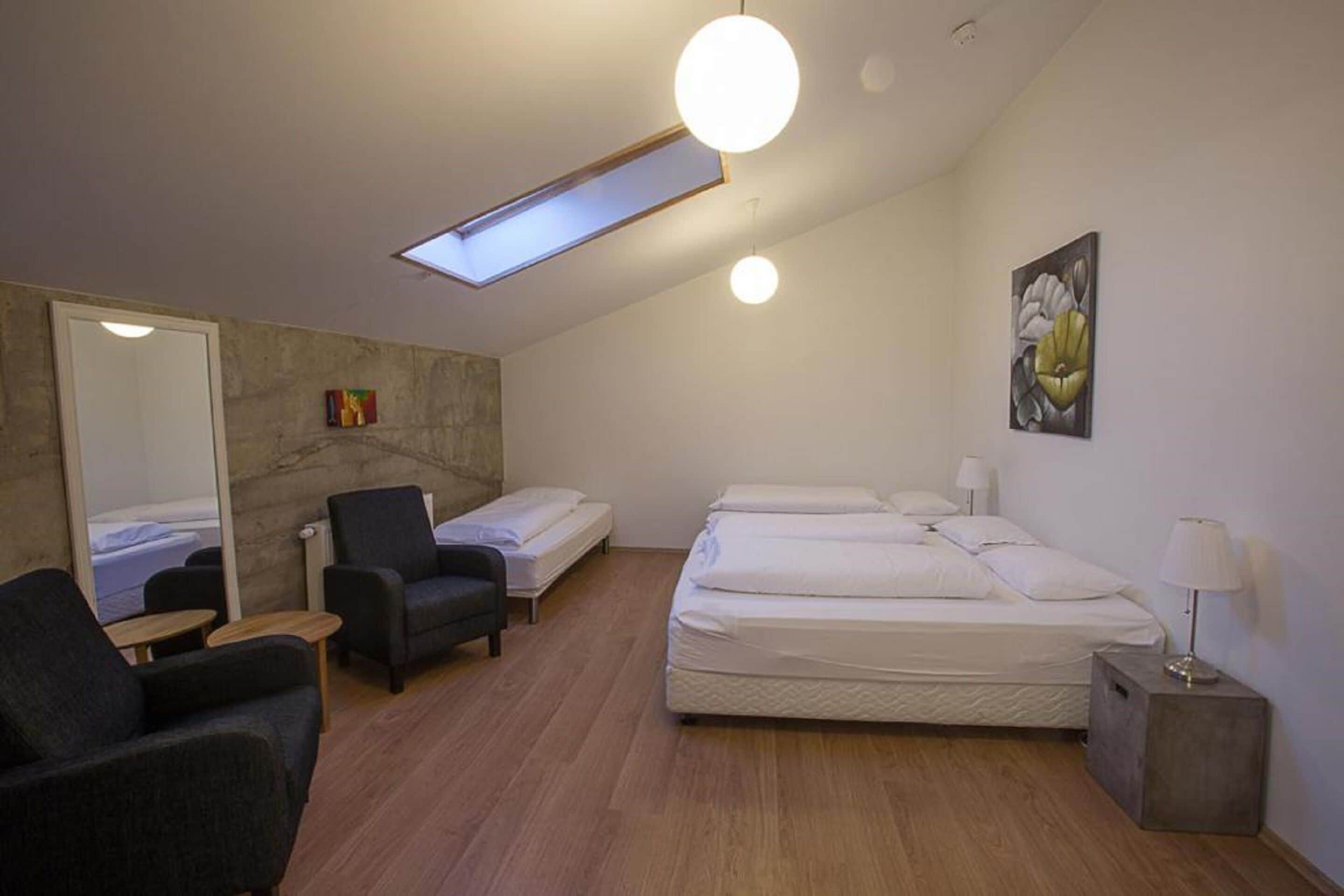 Una habitación de hotel moderna con tragaluz, cama, sillón, mesita y mesita de noche.