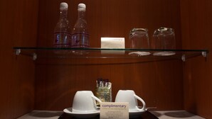 Quarto de hotel com uma prateleira de vidro exibindo garrafas e um aviso de café de cortesia.