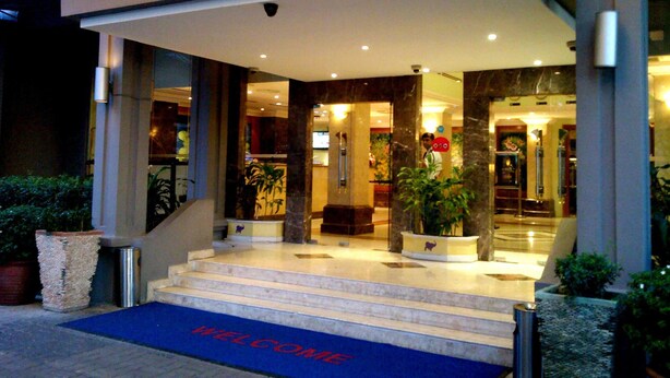 Entrada de hotel com escadaria de mármore, tapete de boas-vindas e vasos de plantas.