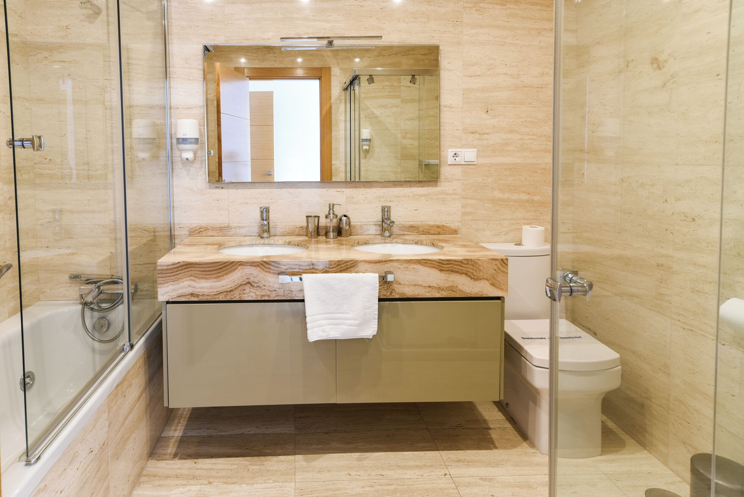 Une salle de bain moderne avec une douche à parois de verre, un comptoir en marbre, des toilettes et un miroir au-dessus du lavabo.