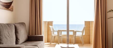 Un salon avec un canapé, une table basse et une vue sur la mer, visible à travers une grande fenêtre.