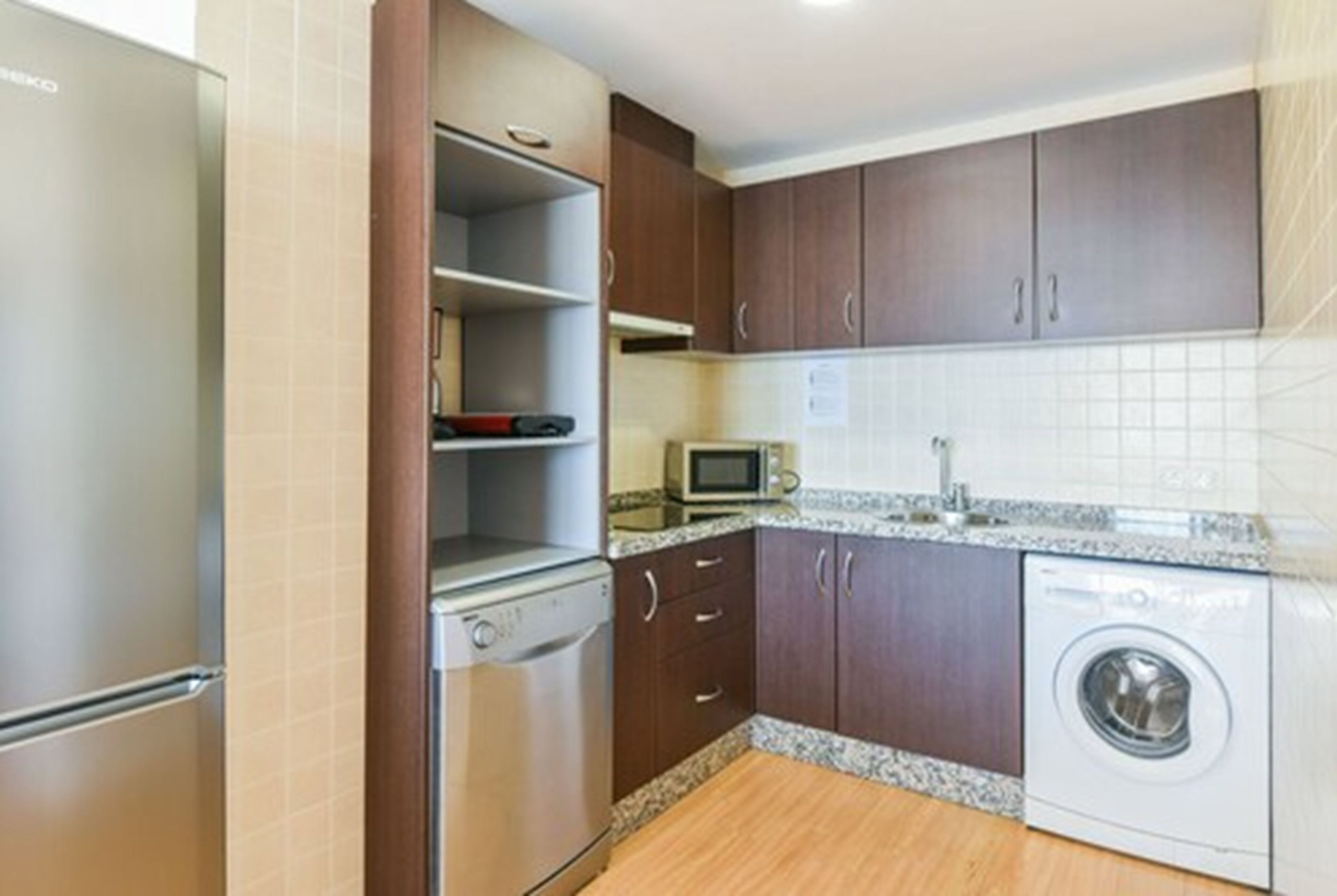 A compact kitchen with a refrigerator, microwave, dishwasher, and washing machine.