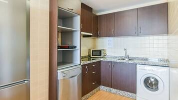 A compact kitchen with a refrigerator, microwave, dishwasher, and washing machine.