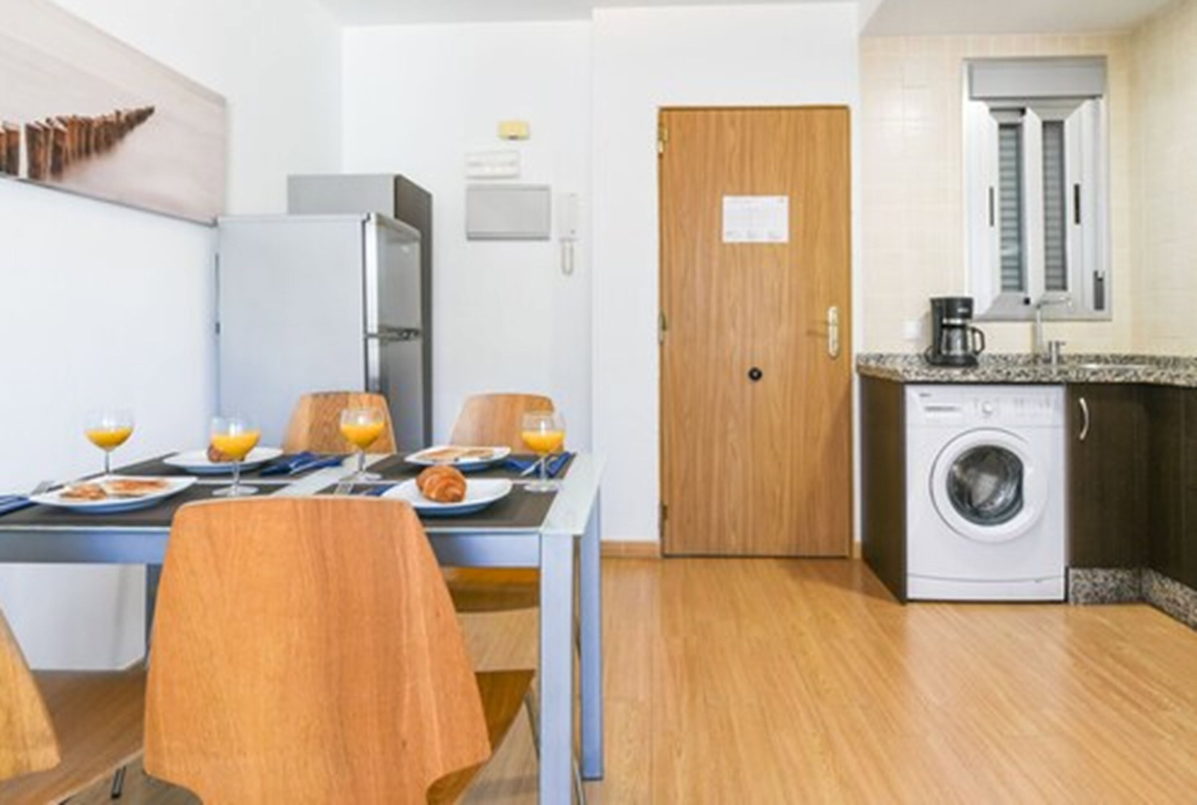 A compact kitchen with a refrigerator, a washing machine, and a dining area with a table set for breakfast.