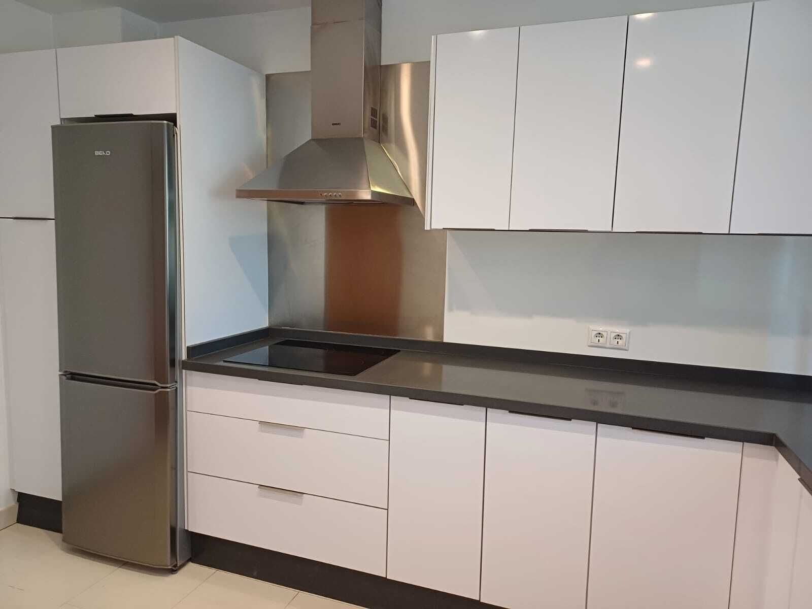 Eine moderne Küche mit weißen Schränken, einem Edelstahlkühlschrank und einer schwarzen Arbeitsplatte.