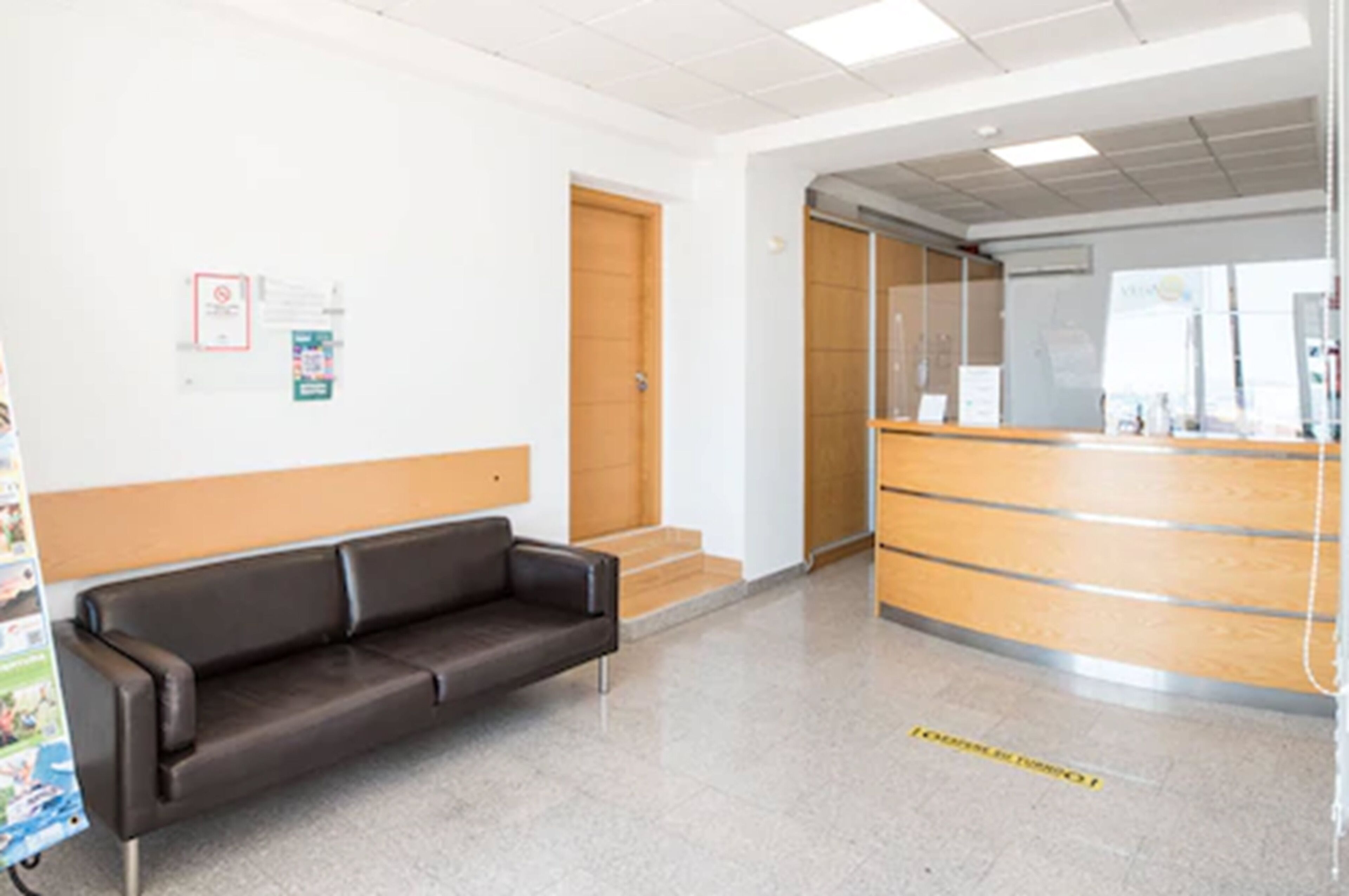 A reception area with a wooden reception desk, a black leather sofa, and a staircase leading to an upper floor.