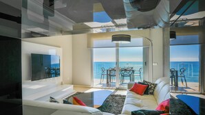 A modern living room with a large TV, a sofa with colorful cushions, and a view of the ocean through large windows. - Apartamentos Vegasol Playa A.T. (Fuengirola)