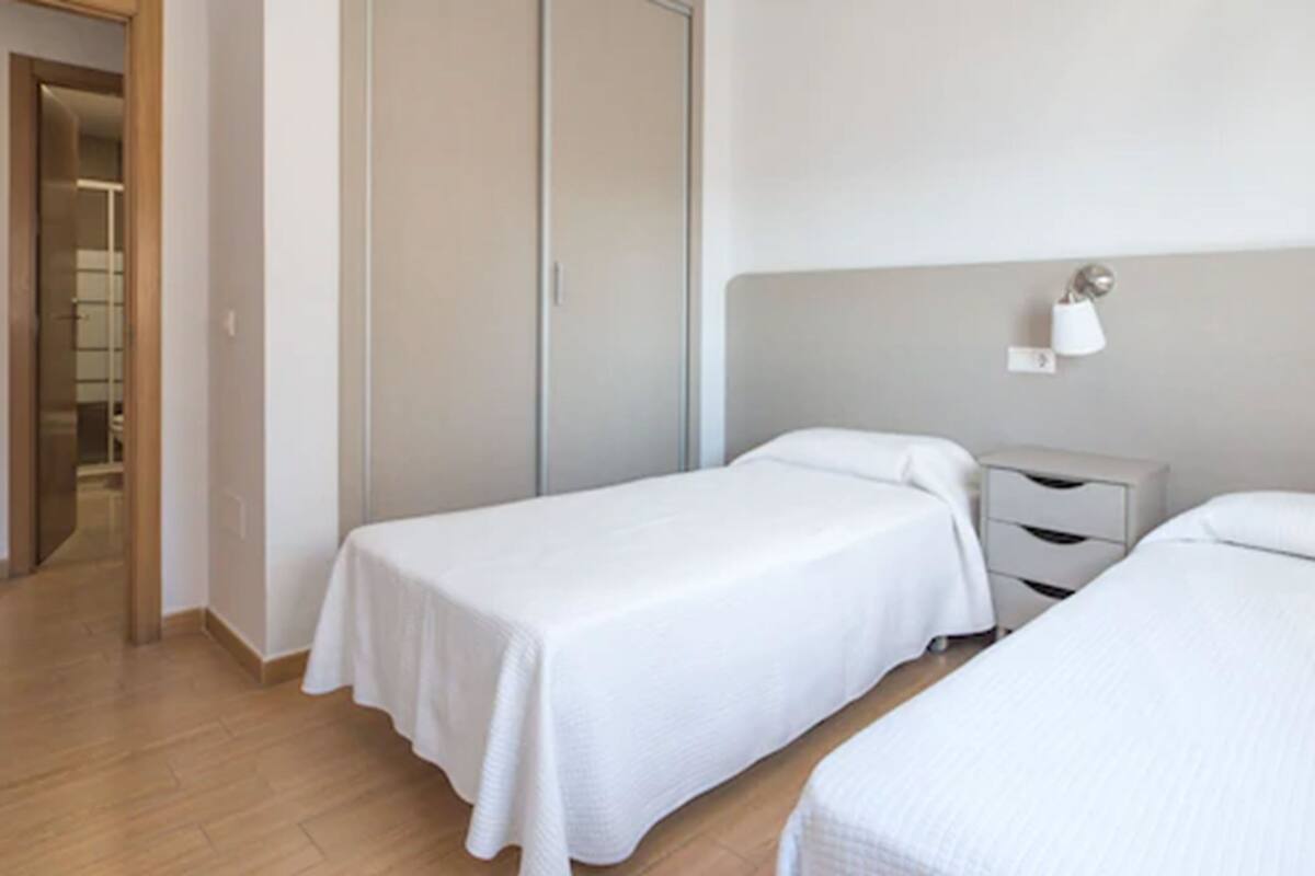 A hotel room with two single beds, a bedside table, a wardrobe, and a mirror.