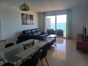 A modern living room with a black leather sofa, a glass dining table, and a view of the sea through large windows. - Apartamentos Vegasol Playa A.T. (Fuengirola)