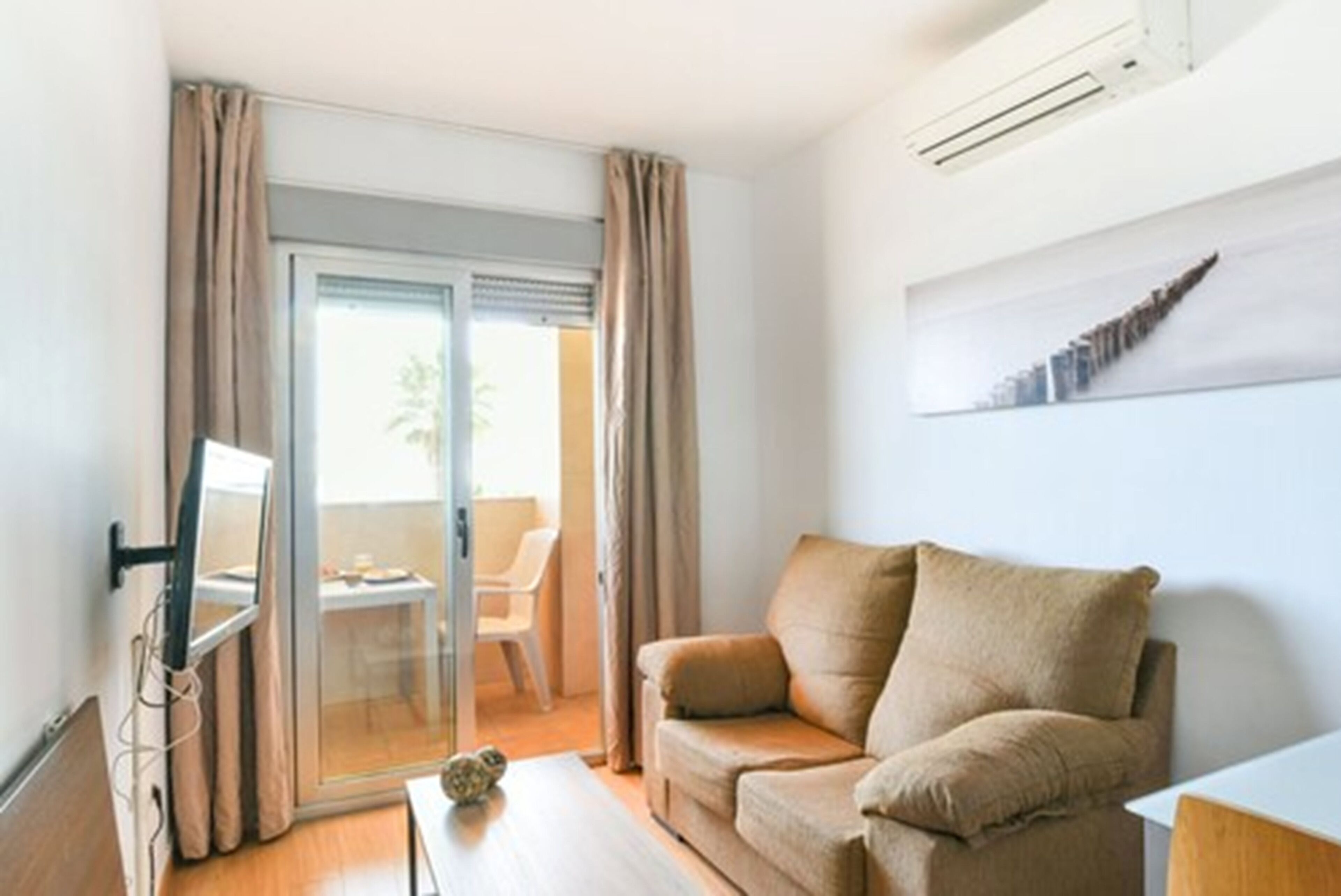 Een moderne woonkamer met een bank, een flatscreen televisie en een schuifpui naar een balkon.