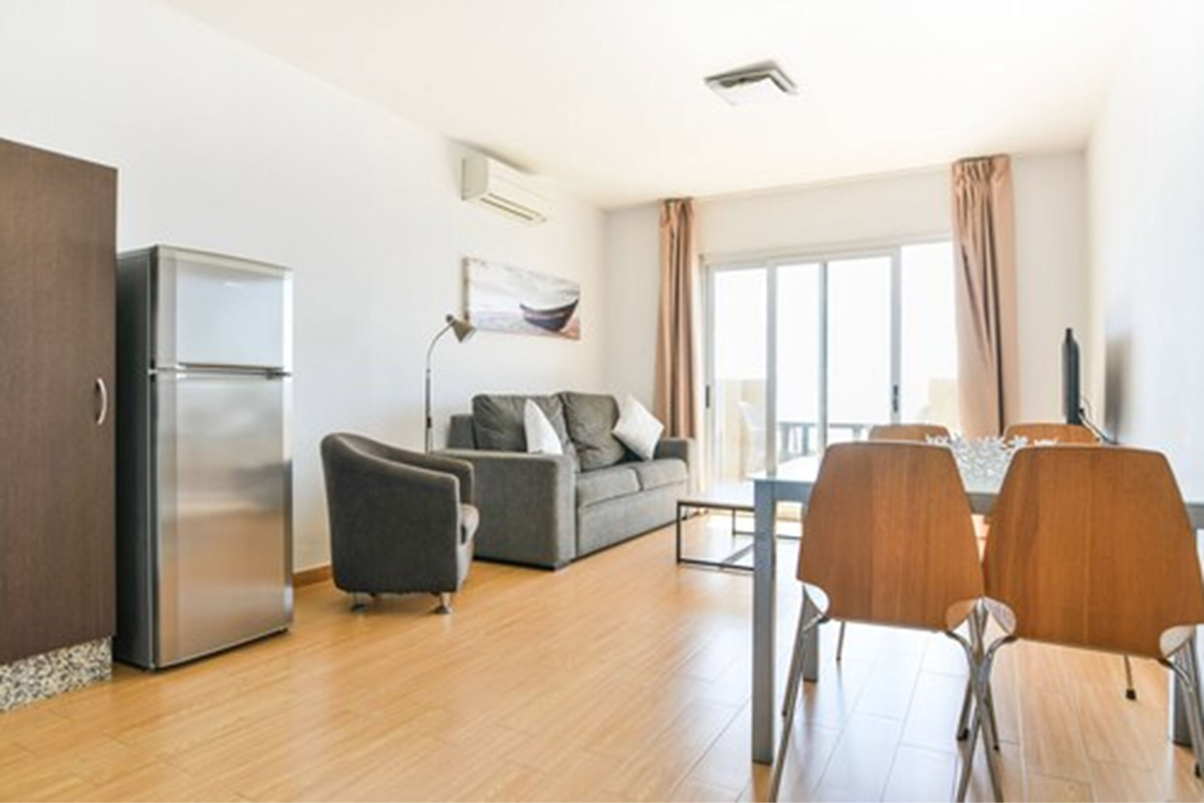 A modern living room with a sofa, a dining table with chairs, a refrigerator, and a window with curtains.