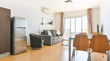 A modern living room with a sofa, a dining table with chairs, a refrigerator, and a window with curtains.