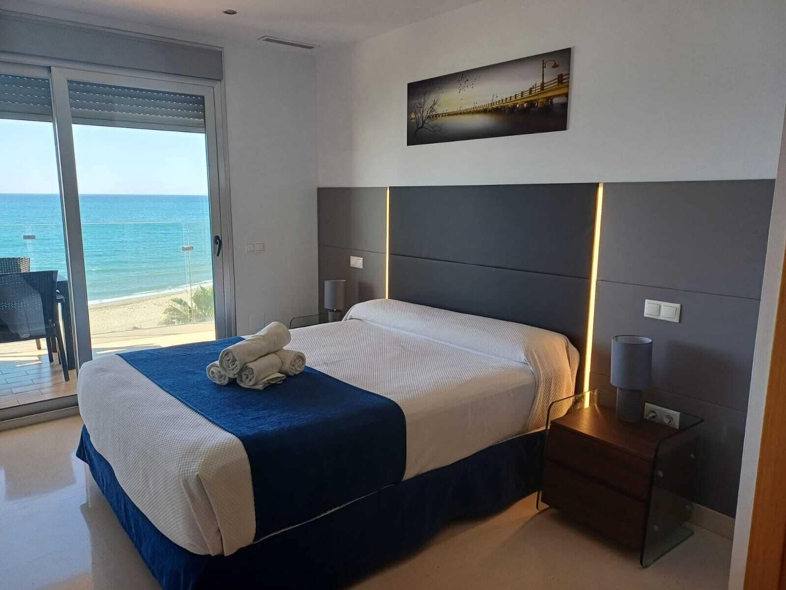 A bedroom with a bed, a nightstand, and a view of the ocean.
