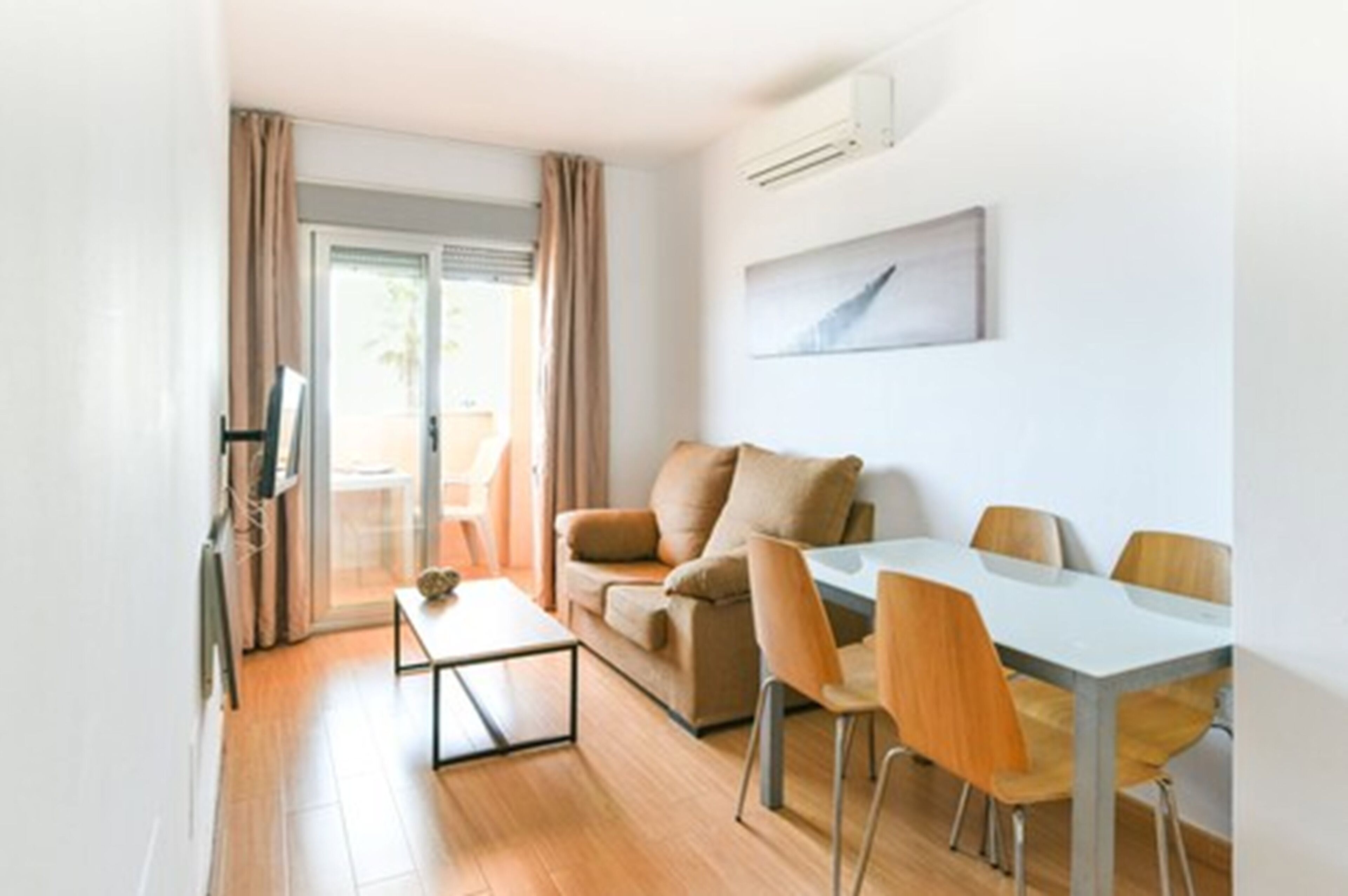 A modern living room with a sofa, dining table, and chairs. There is a sliding glass door leading to a balcony.