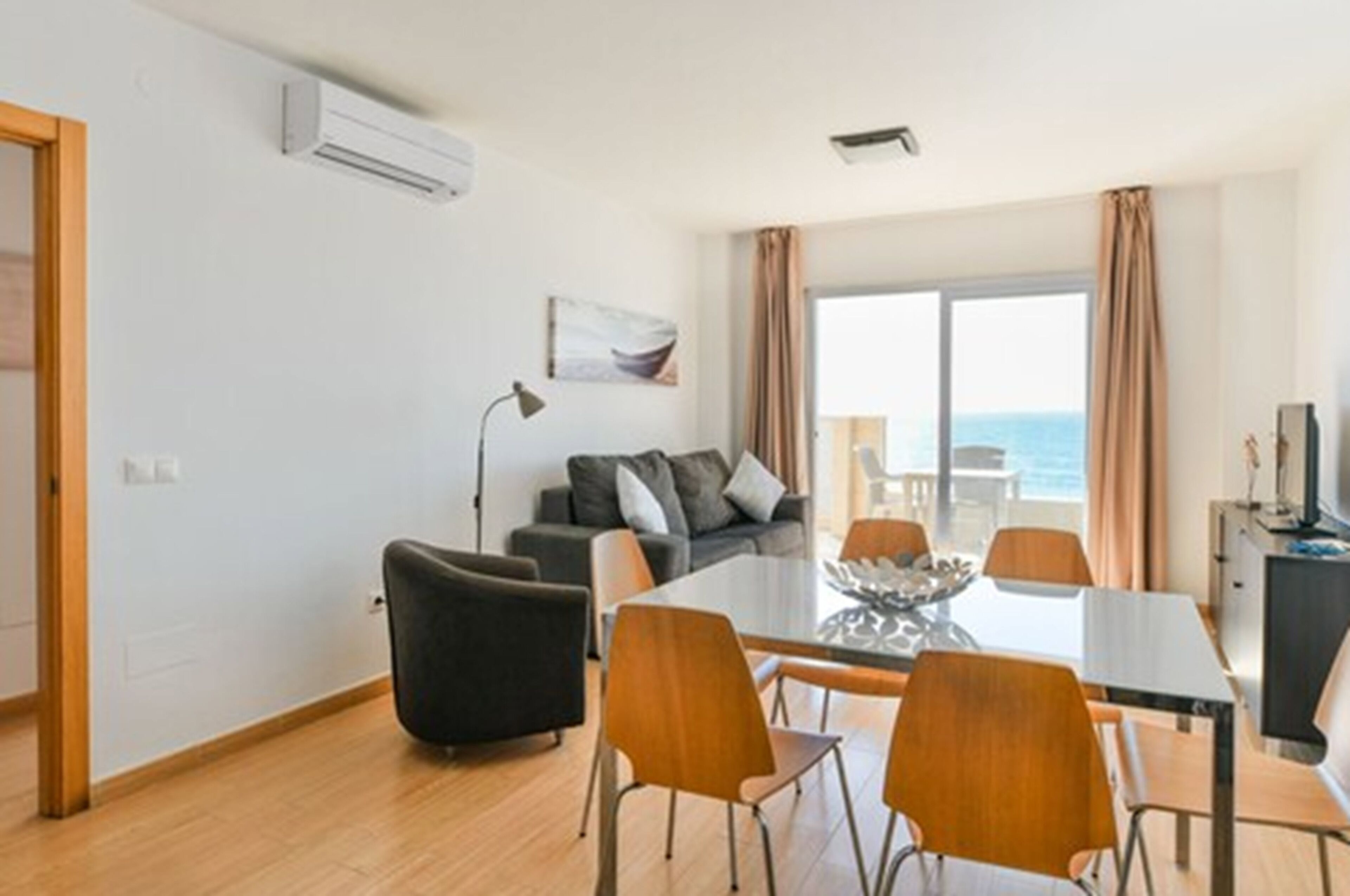Una sala de estar moderna con un sofá, una mesa de comedor con sillas y un ventanal con cortinas.
