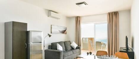 Een moderne woonkamer met een grijze bank, een eettafel met stoelen, een koelkast en een flatscreen-televisie.