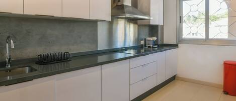 A modern kitchen with white cabinets, a stainless steel range hood, a built-in sink, and a window with a geometric design.