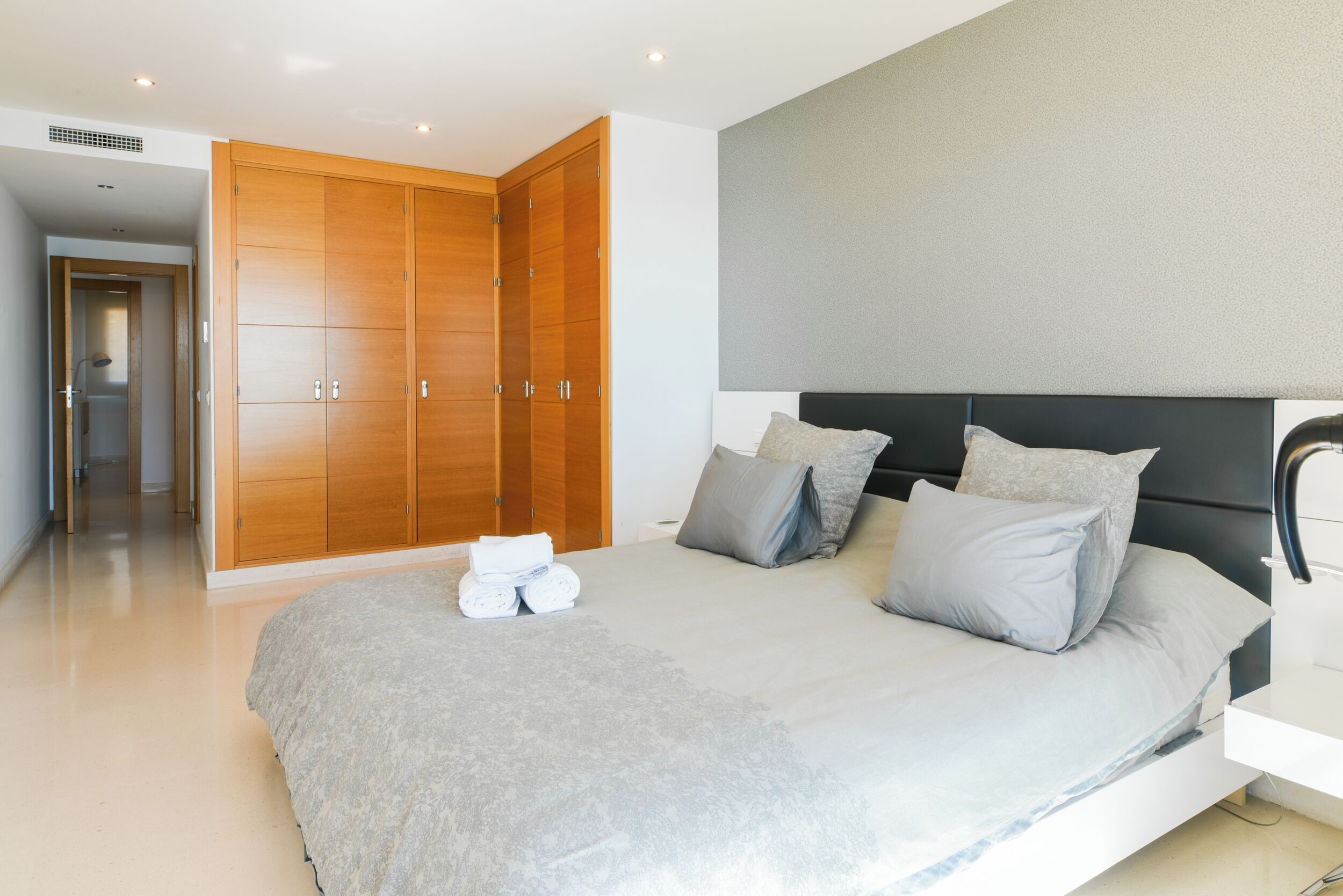 A modern bedroom with a large bed, grey bedding, and a wooden wardrobe.