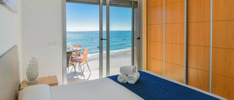 A hotel room with a bed, a view of the beach, and a wooden wardrobe.