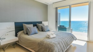 A modern bedroom with a large bed, a bedside table, and a view of the ocean through a sliding glass door. - Apartamentos Vegasol Playa A.T. (Fuengirola)