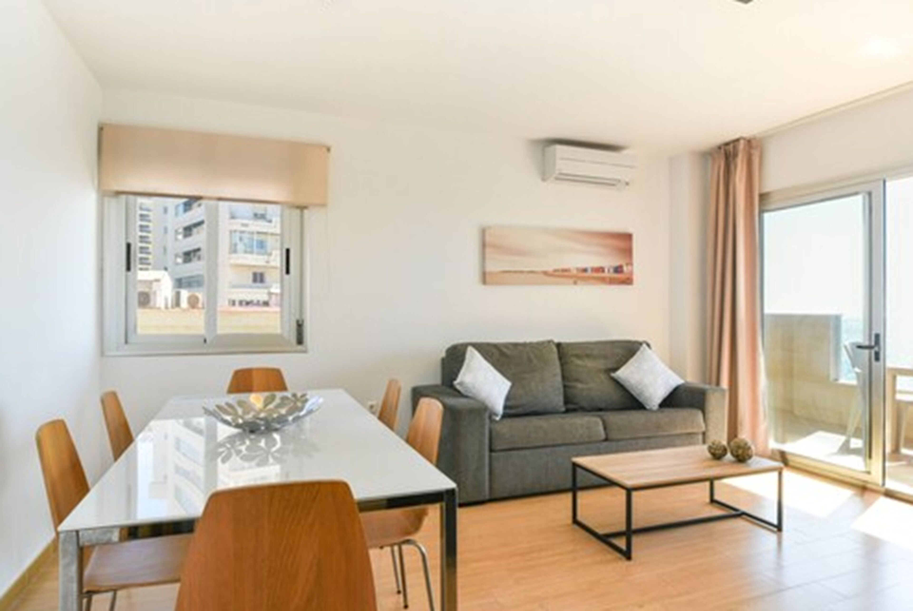 A modern living room with a dining table, sofa, and a view of the city through a large window.