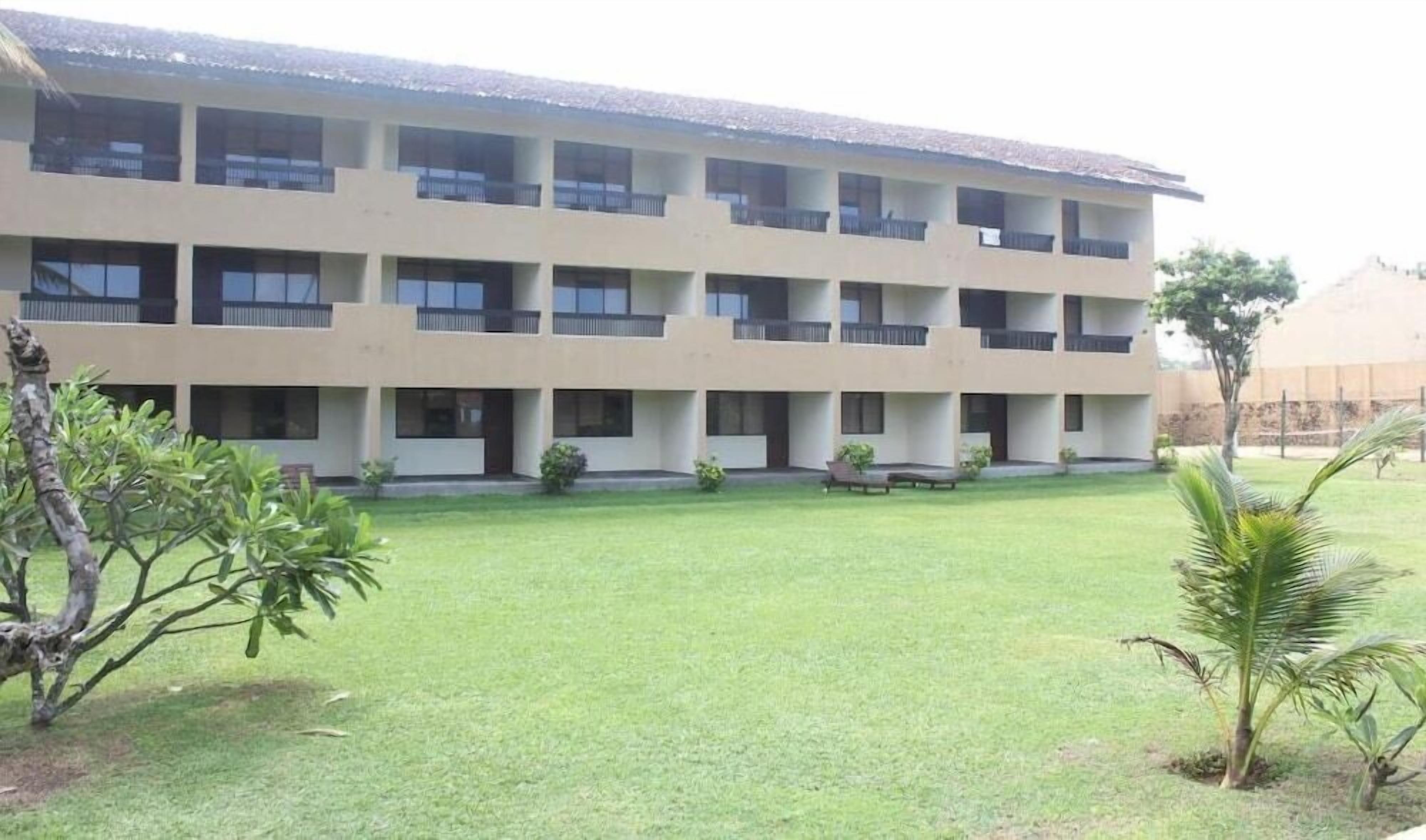 A multi-story building with a flat roof, multiple balconies, and a well-maintained lawn with small trees.