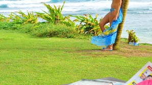 A person standing by a palm tree on a grassy area with a table in the foreground containing magazines and a smartphone. - Club Koggala Village (Koggala)