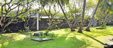 A well-maintained garden with a stone wall, palm trees, and a sign for a bed and breakfast.