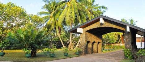 A covered entrance with a stone archway, surrounded by lush greenery and palm trees.