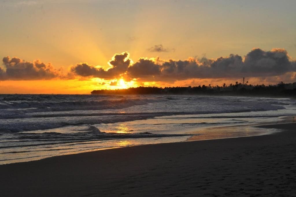 Une plage au coucher du soleil, avec des vagues et une côte lointaine.