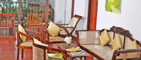A room with wooden furniture, including chairs and a sofa, arranged around a central table with a vase of flowers.